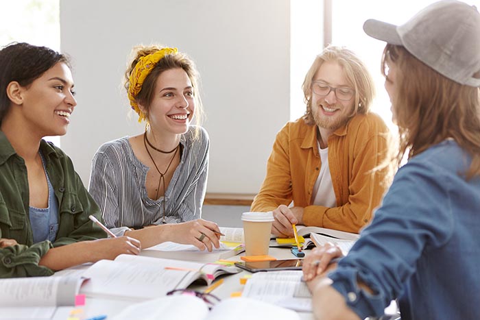 Horizontal portrait of multi-ethnic encouraged students surrounded with books having talk working together preparing for seminar reading books and writing something. People working with books